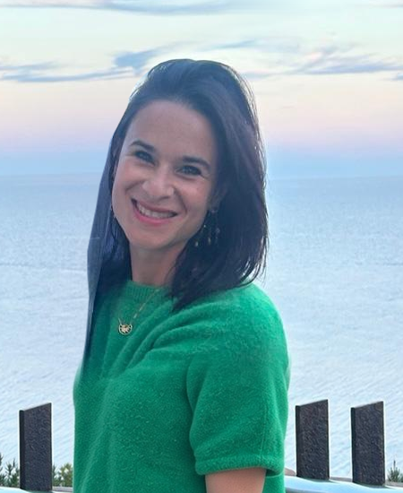 Annelies smiling by the sea in her green top.
